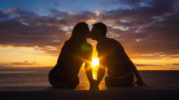 Silueta de una pareja sentada frente al mar besándose durante el atardecer.